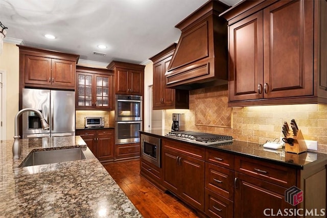 kitchen featuring sink, custom exhaust hood, dark stone counters, and appliances with stainless steel finishes