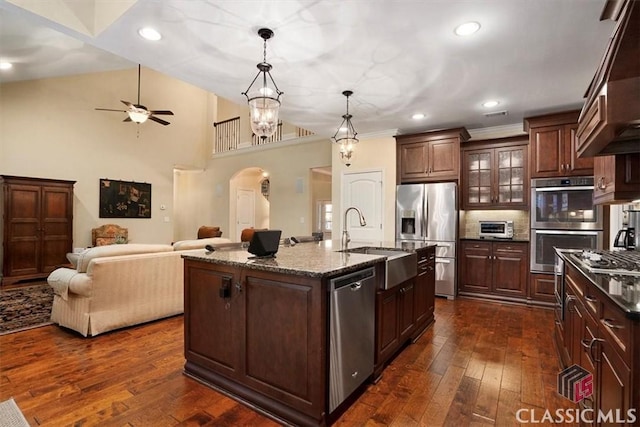 kitchen with pendant lighting, sink, appliances with stainless steel finishes, dark hardwood / wood-style floors, and a center island with sink