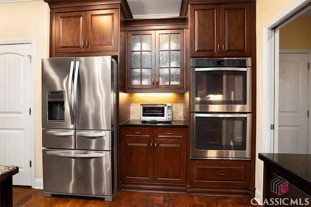 kitchen featuring tasteful backsplash, appliances with stainless steel finishes, dark stone countertops, and dark hardwood / wood-style flooring