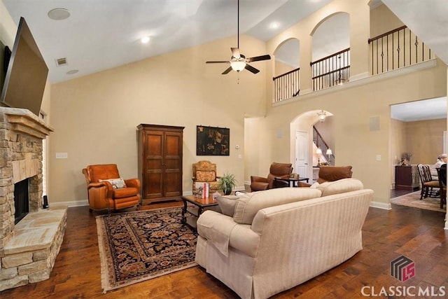 living room with a stone fireplace, dark wood-type flooring, high vaulted ceiling, and ceiling fan