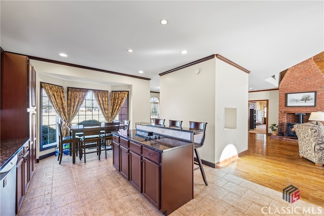 kitchen featuring dishwasher, a brick fireplace, a kitchen bar, and dark stone counters