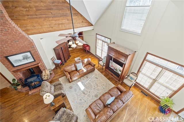 living room featuring hardwood / wood-style flooring, ceiling fan, high vaulted ceiling, and a wood stove