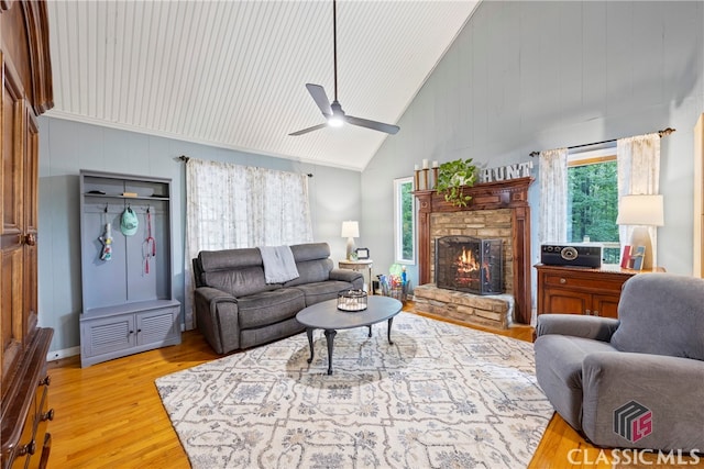 living room featuring ceiling fan, a fireplace, high vaulted ceiling, and light wood-type flooring