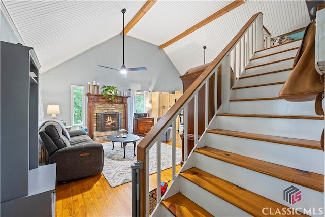 stairway featuring hardwood / wood-style flooring, ceiling fan, high vaulted ceiling, a fireplace, and beamed ceiling