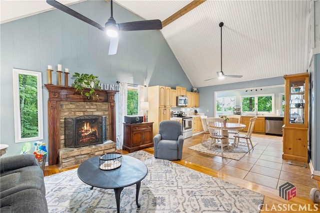 living room featuring ceiling fan, a stone fireplace, high vaulted ceiling, and light tile patterned floors