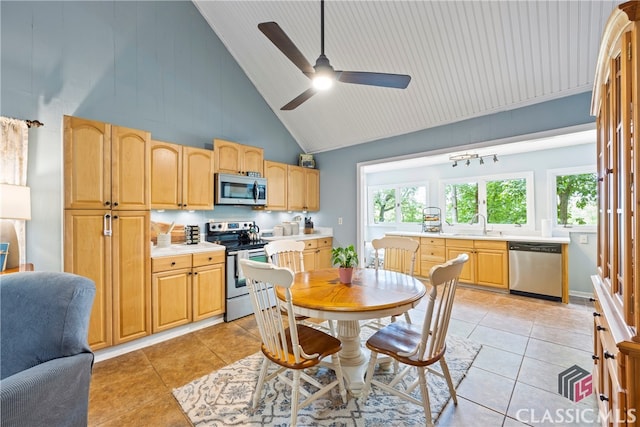 kitchen with appliances with stainless steel finishes, high vaulted ceiling, sink, light tile patterned floors, and ceiling fan