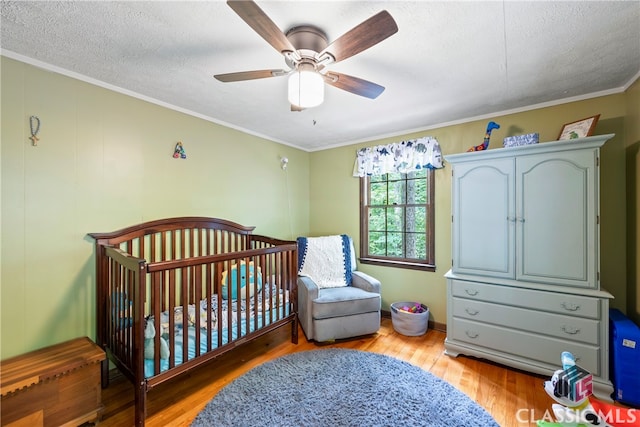 bedroom with a nursery area, wood-type flooring, ceiling fan, crown molding, and a textured ceiling