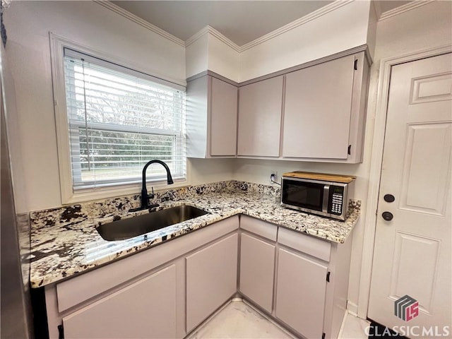 kitchen featuring light stone counters, ornamental molding, and sink