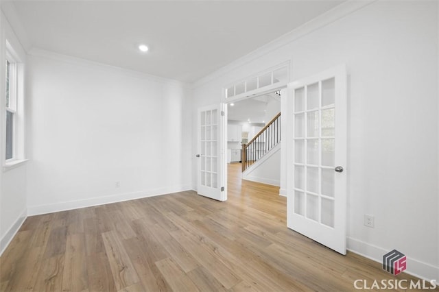 empty room featuring crown molding, light wood-type flooring, and french doors