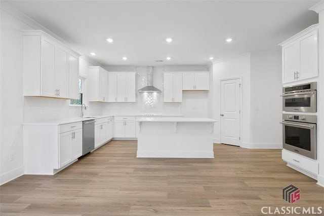 kitchen featuring appliances with stainless steel finishes, wall chimney exhaust hood, a kitchen island, and white cabinets