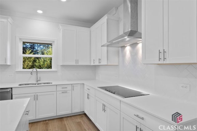 kitchen featuring sink, light hardwood / wood-style flooring, white cabinetry, black electric stovetop, and wall chimney exhaust hood