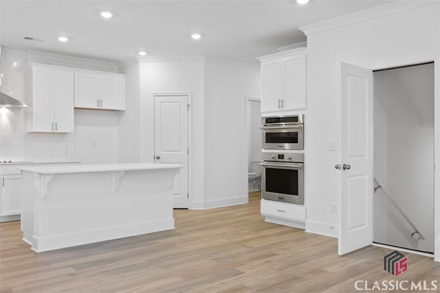 kitchen featuring white cabinetry, crown molding, light hardwood / wood-style flooring, double oven, and a kitchen island