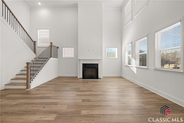 unfurnished living room featuring crown molding, a towering ceiling, and light hardwood / wood-style floors