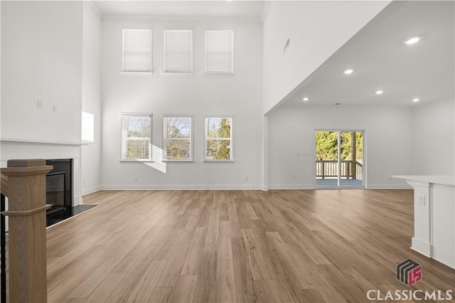 unfurnished living room featuring ornamental molding, light hardwood / wood-style flooring, and a high ceiling