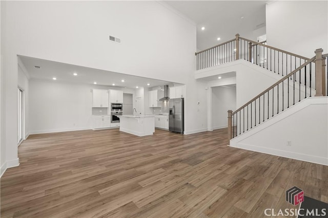 unfurnished living room with a high ceiling, ornamental molding, sink, and hardwood / wood-style floors