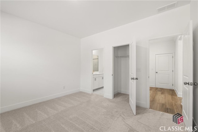 unfurnished bedroom featuring light colored carpet, ensuite bath, and a closet