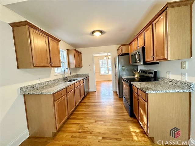 kitchen with light stone countertops, appliances with stainless steel finishes, sink, and light wood-type flooring