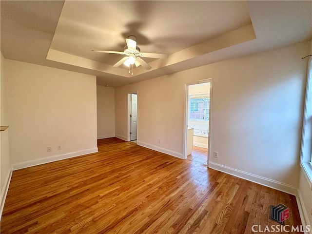 empty room with ceiling fan, a tray ceiling, and light hardwood / wood-style floors