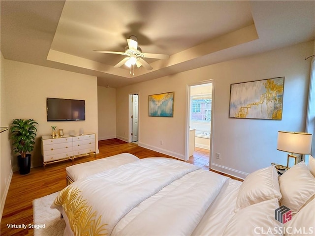 bedroom with hardwood / wood-style flooring, ensuite bath, a raised ceiling, and ceiling fan