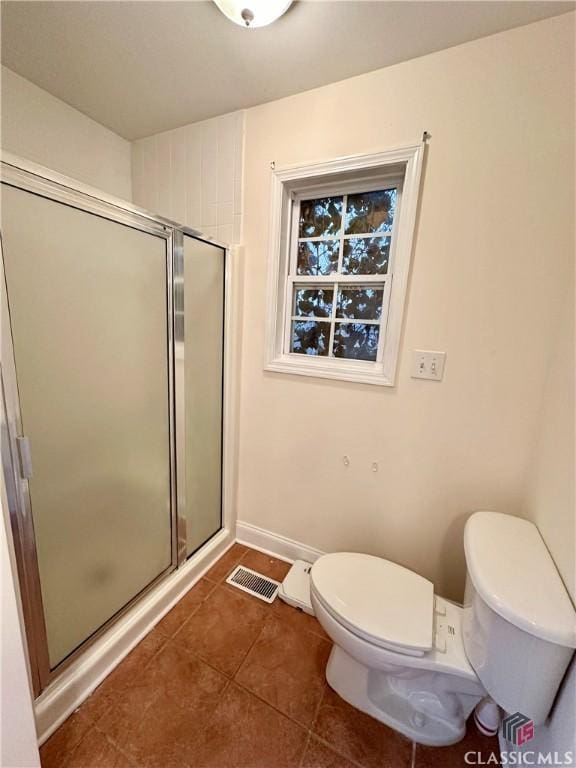 bathroom featuring toilet, a shower with shower door, and tile patterned flooring