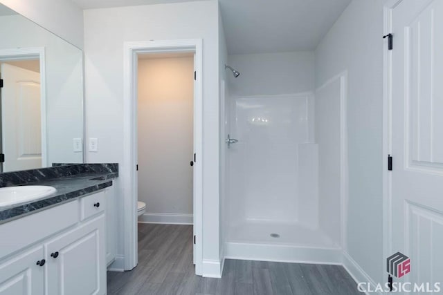 bathroom featuring hardwood / wood-style flooring, a shower, vanity, and toilet