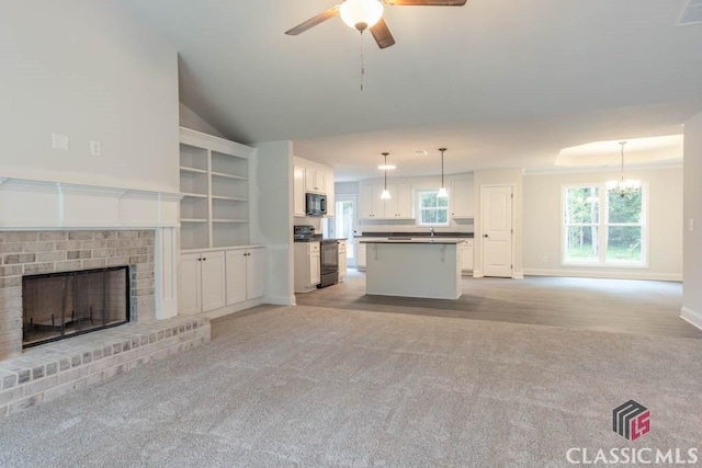 unfurnished living room with lofted ceiling, sink, a fireplace, light carpet, and ceiling fan with notable chandelier