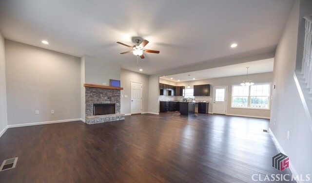 unfurnished living room with dark hardwood / wood-style flooring, ceiling fan with notable chandelier, and a fireplace