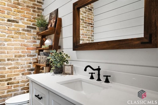 bathroom featuring brick wall, vanity, and toilet