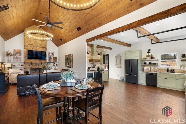 dining area featuring a stone fireplace, dark wood-type flooring, vaulted ceiling with beams, and wooden ceiling