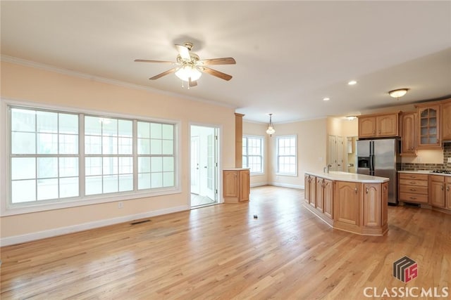 kitchen featuring stainless steel refrigerator with ice dispenser, ornamental molding, a kitchen island, and light wood-type flooring