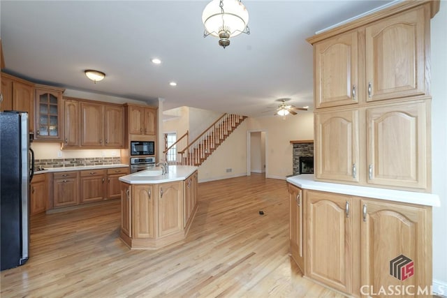 kitchen with light hardwood / wood-style flooring, ceiling fan, hanging light fixtures, stainless steel appliances, and an island with sink