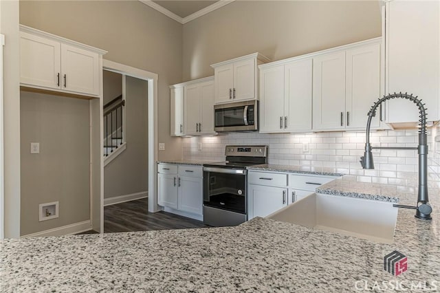 kitchen featuring appliances with stainless steel finishes, white cabinetry, backsplash, light stone counters, and ornamental molding