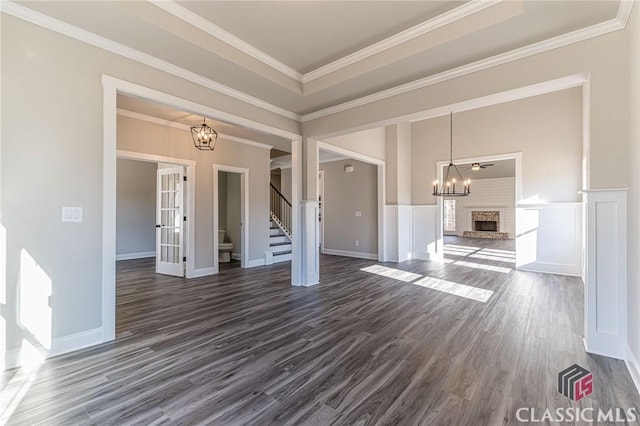 unfurnished living room with ornamental molding, dark hardwood / wood-style floors, a raised ceiling, and a notable chandelier