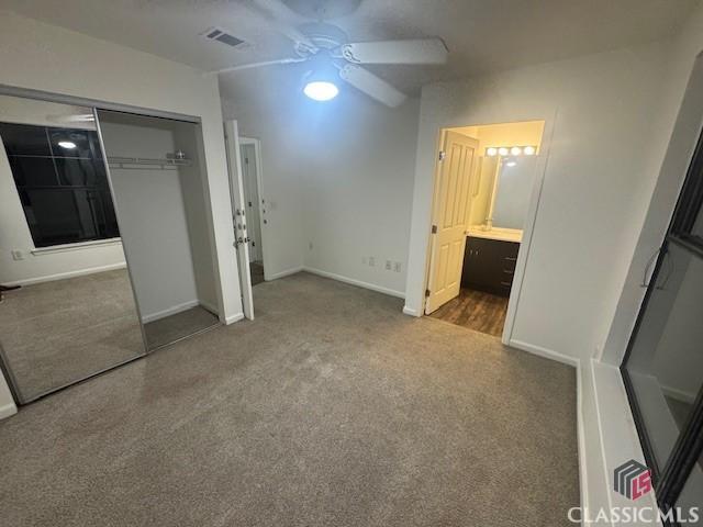 unfurnished bedroom featuring ensuite bathroom, ceiling fan, a closet, and dark carpet