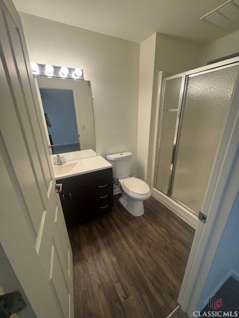 bathroom featuring toilet, hardwood / wood-style flooring, vanity, and a shower with door