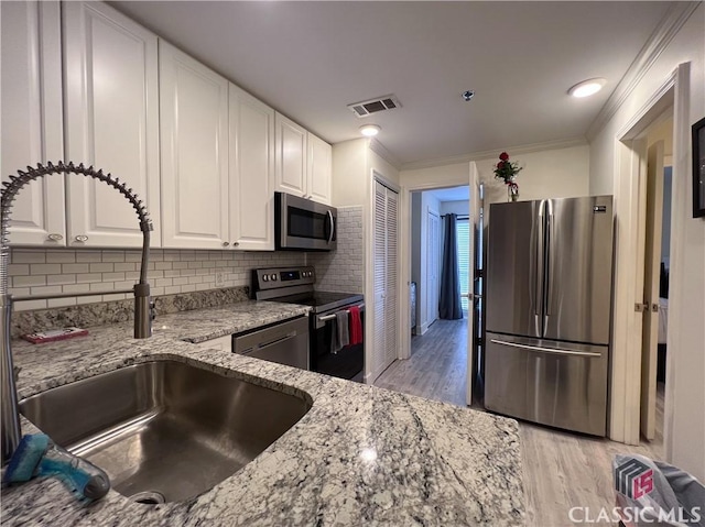 kitchen featuring sink, white cabinets, light stone counters, stainless steel appliances, and light wood-type flooring