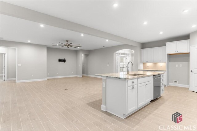 kitchen with sink, light stone countertops, an island with sink, and white cabinets