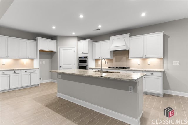 kitchen featuring white cabinetry, a kitchen island with sink, and custom exhaust hood