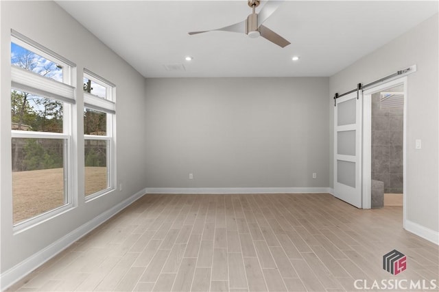 unfurnished room with ceiling fan, a barn door, and light hardwood / wood-style floors