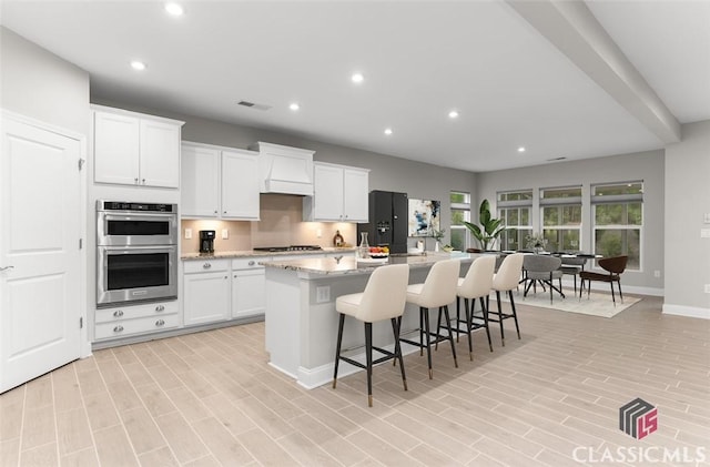 kitchen with white cabinets, a kitchen breakfast bar, stainless steel appliances, light stone countertops, and a center island with sink