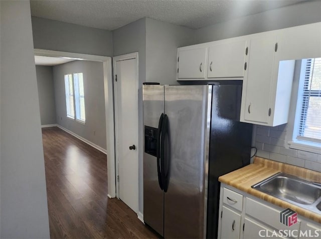 kitchen with dark wood-type flooring, white cabinetry, stainless steel refrigerator with ice dispenser, a wealth of natural light, and decorative backsplash