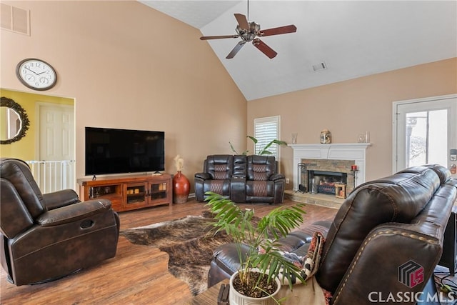 living room with hardwood / wood-style flooring, a stone fireplace, high vaulted ceiling, and ceiling fan