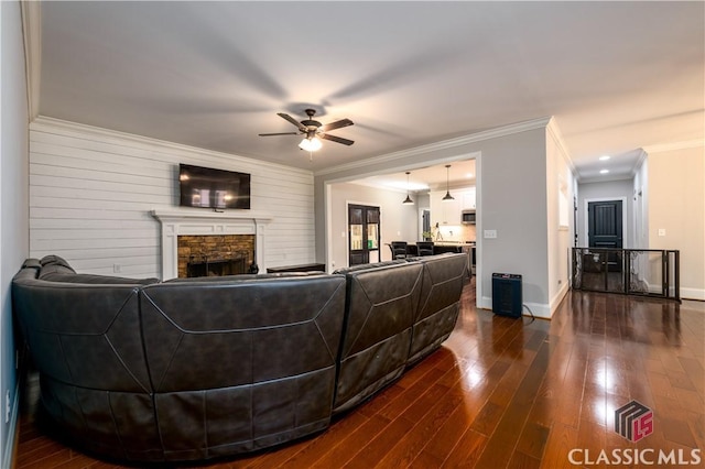 living room with dark wood-type flooring, ceiling fan, ornamental molding, and a fireplace