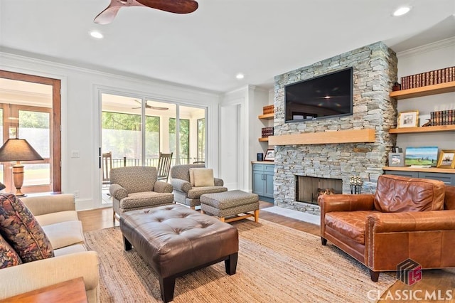 living room featuring ceiling fan, ornamental molding, a stone fireplace, and light hardwood / wood-style flooring