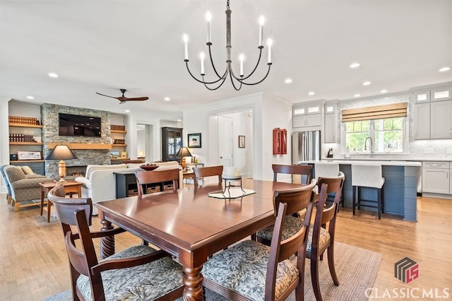 dining area featuring ceiling fan, a fireplace, sink, and light hardwood / wood-style flooring