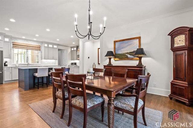 dining space with an inviting chandelier, ornamental molding, wood-type flooring, and sink