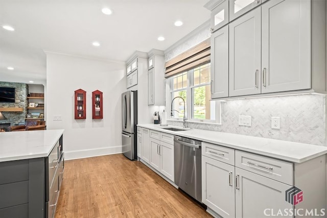 kitchen featuring sink, backsplash, stainless steel appliances, light hardwood / wood-style floors, and a stone fireplace