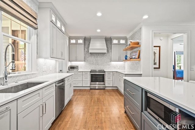 kitchen featuring sink, gray cabinetry, stainless steel appliances, wall chimney range hood, and light hardwood / wood-style flooring