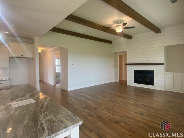 216 Montview Dr, Jefferson, GA 30549 - unfurnished living room featuring ceiling fan, dark wood-style flooring, beam ceiling, a large fireplace, and baseboards