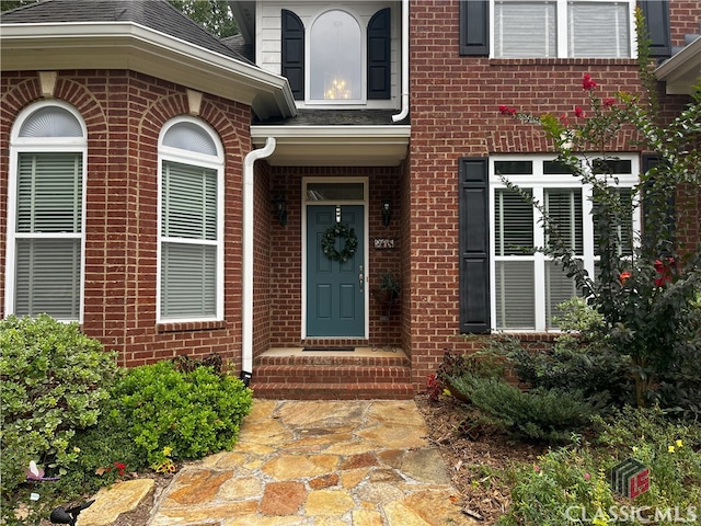 property entrance featuring brick siding and roof with shingles